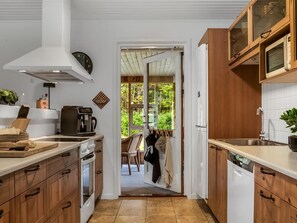 A kitchen with wooden cabinets, a coffee machine, and a view through an open door to a dining area. - "Linnea" -  from the sea by Interhome (Hals)