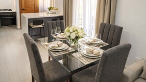 Een eetruimte met een glazen tafel, grijs gestoffeerde stoelen en een vaas witte bloemen.
