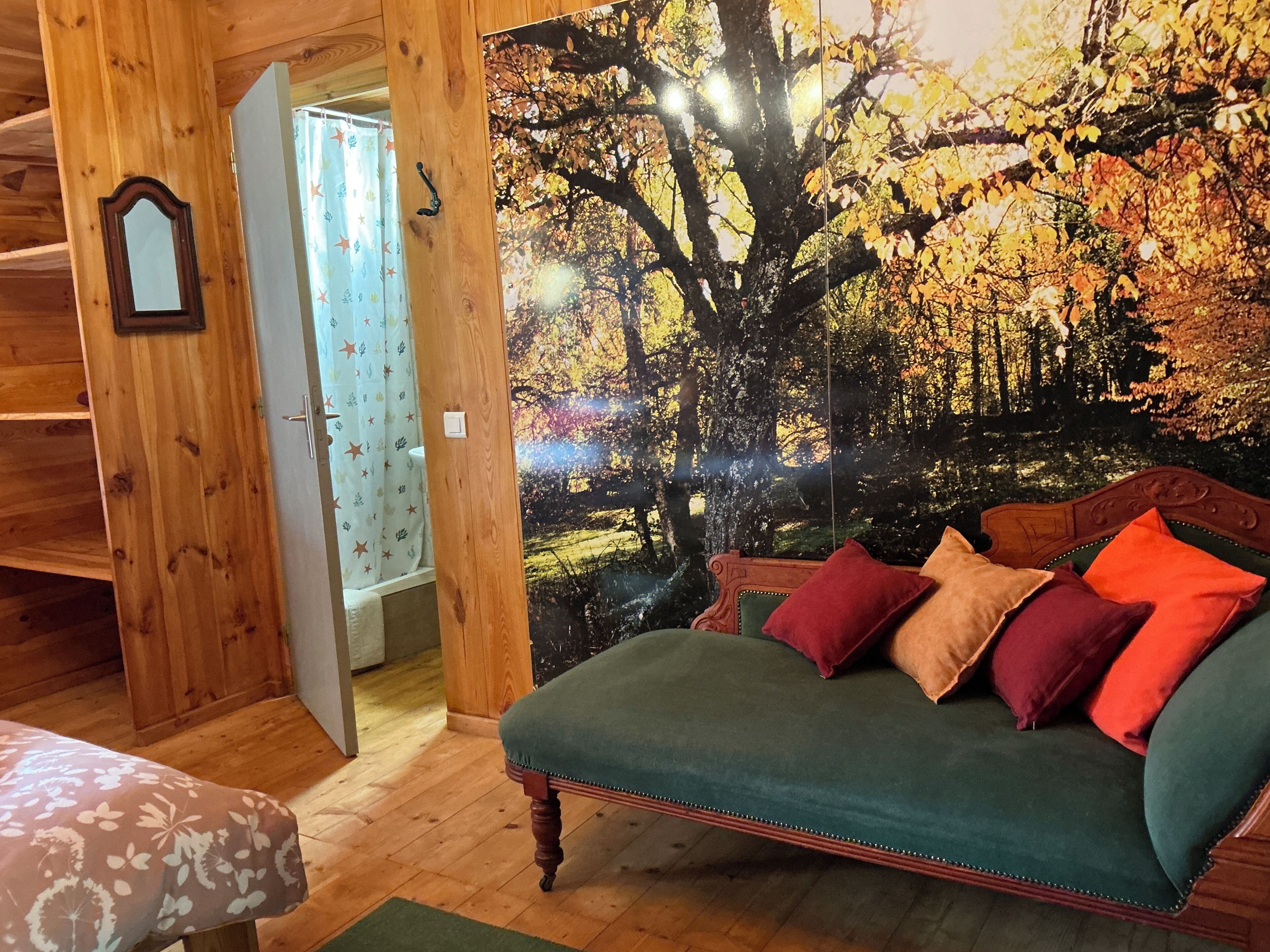 A room with a wooden interior, a green sofa with multiple cushions, a wooden door, and a large wall mural of a forest scene.