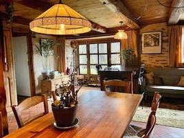 Una mesa de madera con sillas, una lámpara colgante, una ventana con cortinas y un sofá en un interior rústico.