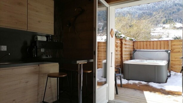 A compact kitchen with wooden cabinets, a coffee maker, and a bar stool. - Apartment DAHU Domaine du Fraizier Thônes private jacuzzi annecy and shops (Thônes)