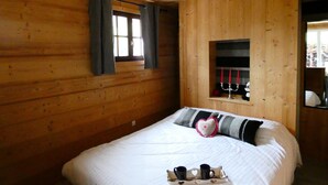 A wooden cabin bedroom with a bed, a window with curtains, a shelf with candles, and a tray with cups. - Apartment DAHU Domaine du Fraizier Thônes private jacuzzi annecy and shops (Thônes)