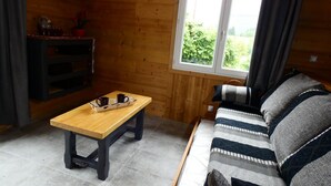 A cozy room with a wooden floor, a sofa with a patterned blanket, a wooden table with a tray of mugs, a mounted air conditioner, and a window with curtains. - Apartment DAHU Domaine du Fraizier Thônes private jacuzzi annecy and shops (Thônes)