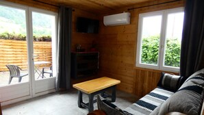 A cozy room with a wooden ceiling, a sofa, a table, a TV, and a window overlooking greenery. - Apartment DAHU Domaine du Fraizier Thônes private jacuzzi annecy and shops (Thônes)