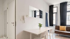 Una habitación moderna con un escritorio blanco, un sofá marrón, una planta en maceta y un espejo grande en la pared.