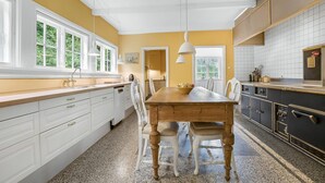 Una cocina con mesa de madera, armarios blancos y vistas a zonas verdes.