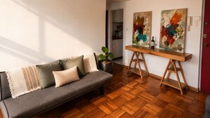 A modern living room with a grey sofa, wooden flooring, and two abstract paintings on easels. - Luminous Home Studio with privileged view to the Park. Steps away from Metro Bilbao. Wifi (Providencia)