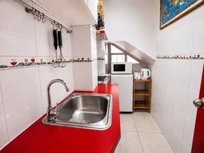 Uma cozinha compacta com uma pia de aço inoxidável, micro-ondas e torradeira sobre uma bancada branca.
