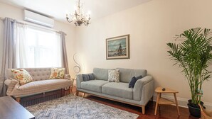 Een woonkamer met een bank, een bijzettafeltje, een plant in pot, een schilderij aan de muur en een kroonluchter.