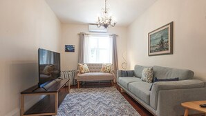 Een woonkamer met een bank, een televisie, een kroonluchter en een schilderij aan de muur.