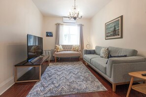 Ein Wohnzimmer mit einer Couch, einem Fernseher, einer Chandelier und einem Gemälde an der Wand.