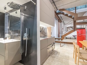 A modern kitchen with a built-in oven, a stainless steel refrigerator, and a dining area with a wooden table and chairs. - Immerse in Barcelona – 2 & 3 Bedroom Units with Terrace Options (Barcelona)