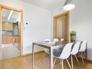 A modern kitchen with wooden cabinets, a sink, and a countertop. There is a dining area with a table and four chairs. A potted plant is on the table. - Immerse in Barcelona – 2 & 3 Bedroom Units with Terrace Options (Barcelona)