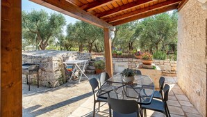 Un patio exterior con una pérgola de madera, paredes de piedra y una mesa con sillas.