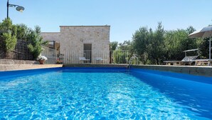 Una piscina con un edificio de piedra al fondo, rodeada de árboles y una valla metálica.