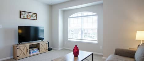 A living room with a flat-screen TV, a coffee table, a sofa, a ceiling fan, and a large window.