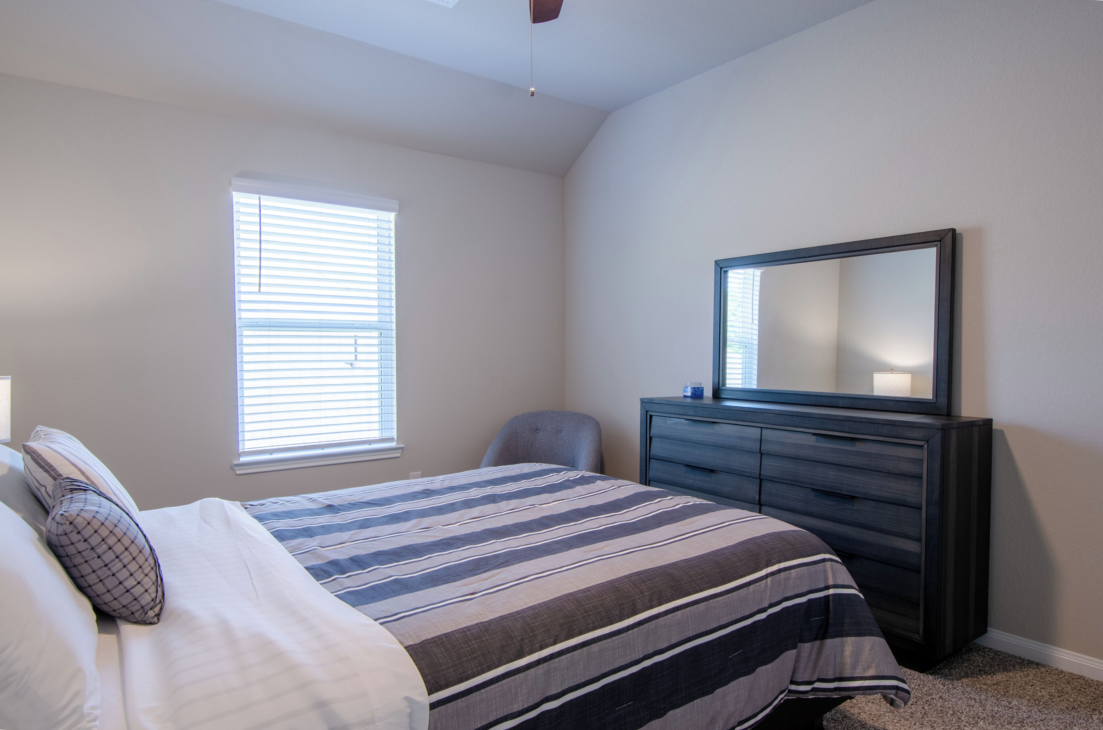Un dormitorio con cama, cómoda, silla y ventana con persianas.