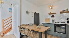 Eine moderne Küche mit Esstisch aus Holz, Korbstühlen, einer Uhr und einem Herd.
