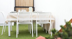 Uma sala de jantar com uma mesa posta para quatro pessoas, cadeiras brancas e um painel de parede de madeira.