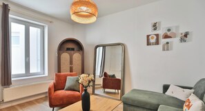 Ein Zimmer mit einem großen Spiegel, einem Holzschrank, einem roten Sessel, einem grünen Sofa und einer Vase mit Blumen.