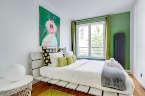 Ein Schlafzimmer mit Bett, Kissen, einem Gemälde, einem Fenster und einer Heizung.