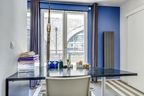 Ein modernes Zimmer mit einem Glastisch, einem Sessel, einem Fenster mit Vorhängen und Blick auf Gebäude.