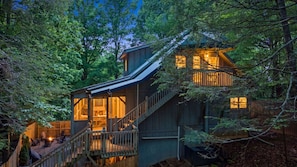 A wooden cabin with a staircase leading to a deck, surrounded by trees. - Log Hollow | Hot Tub, Plenty of Games, Play Area! (Townsend)