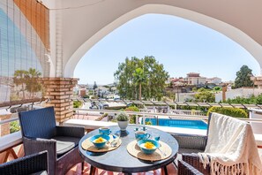 Un balcon agrémenté de meubles en osier, une table dressée avec des bols et des tasses bleus, et une vue sur une piscine et des immeubles.