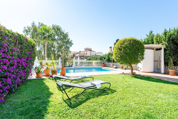 Zona de piscina con piscina, sillas de descanso y valla blanca.