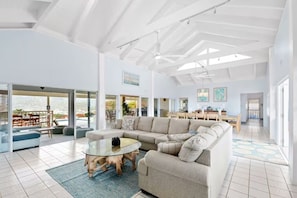 A spacious living area with a large sectional sofa, a glass coffee table, and a dining area in the background.