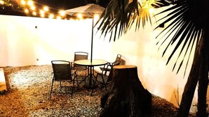 Eine Terrass mit Tisch und Stühlen, umgeben von Kies und einer Palme.