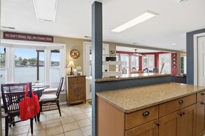 A kitchen with a granite countertop, wooden cabinets, a dining area with a table and chairs, and a view of the water outside. - Lakefront Home With Stunning Lake Views (Sunrise Beach)