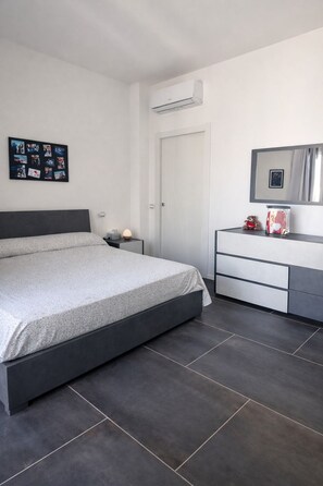 Ein modernes Schlafzimmer mit Bett, Nachttisch, Kommode, Spiegel und Klimaanlage.