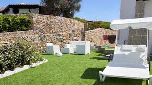 En velholdt græsplæne med udendørs siddepladser, en stenvæg og en moderne bygning.