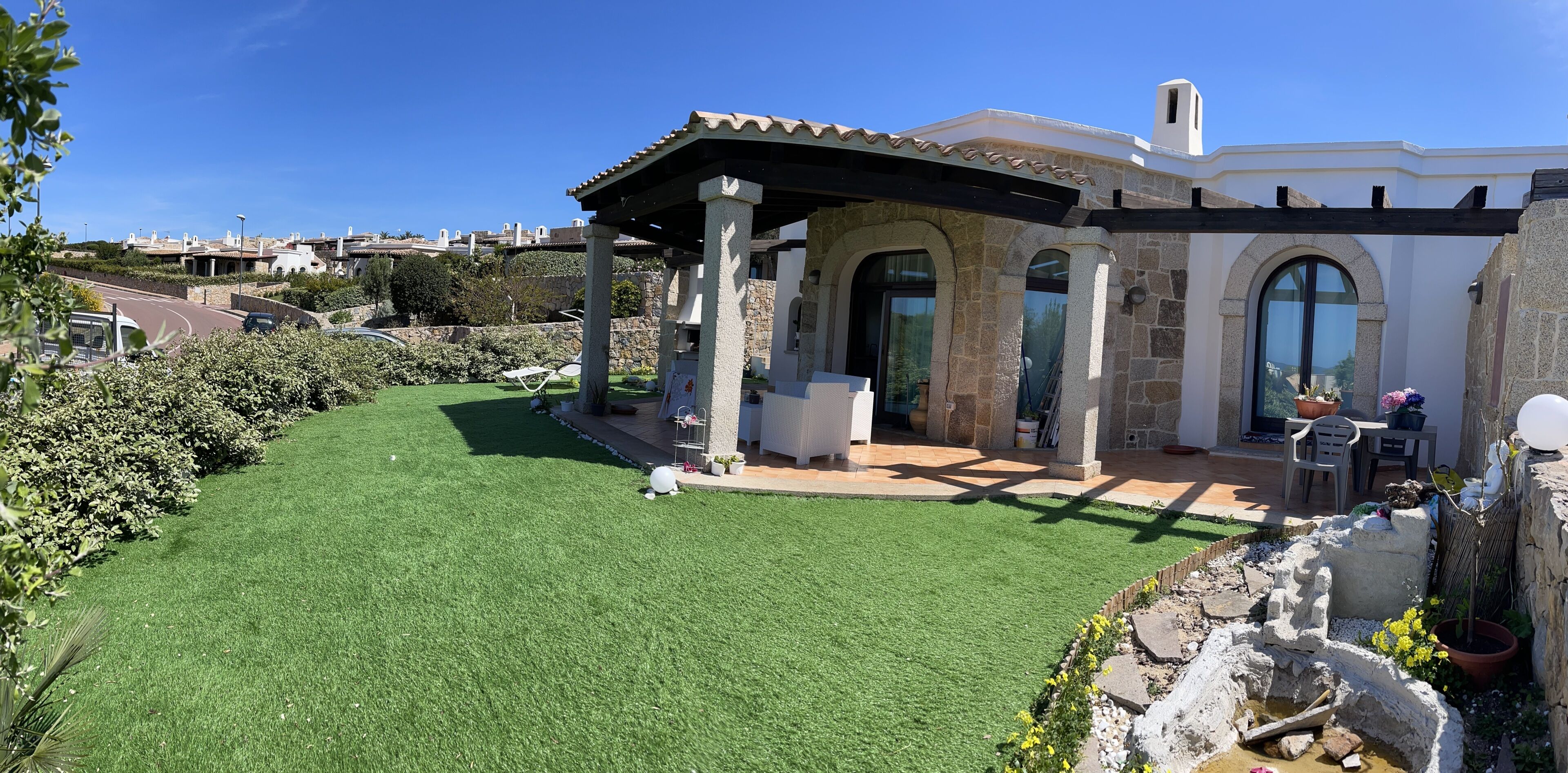 Une maison avec une façade en pierre, un patio couvert et une pelouse bien entretenue.