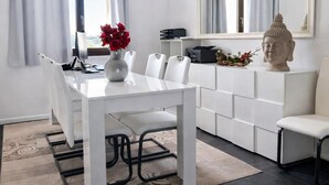 Et moderne køkken med spisebord, stole, en vase med blomster, en Buddha-figur og et stort vindue med gardiner.