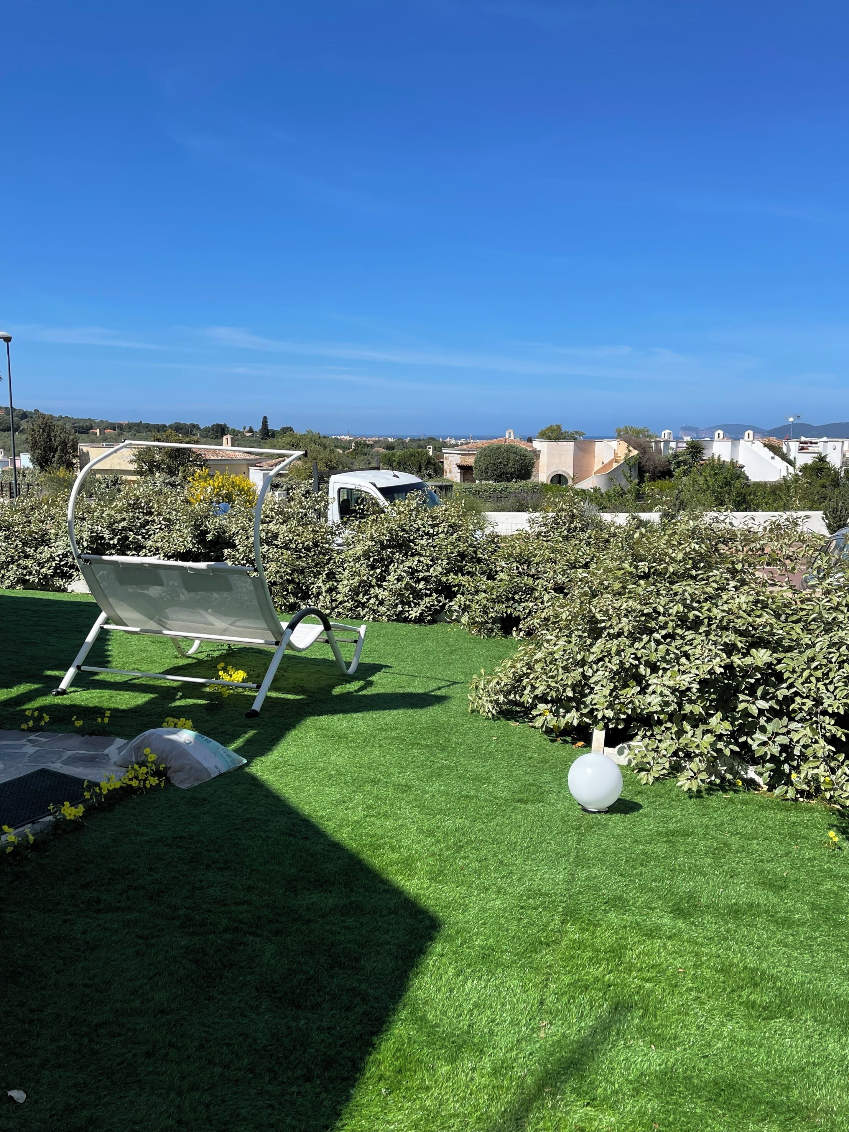 A rooftop garden with artificial grass, a white chair, and a spherical light fixture.
