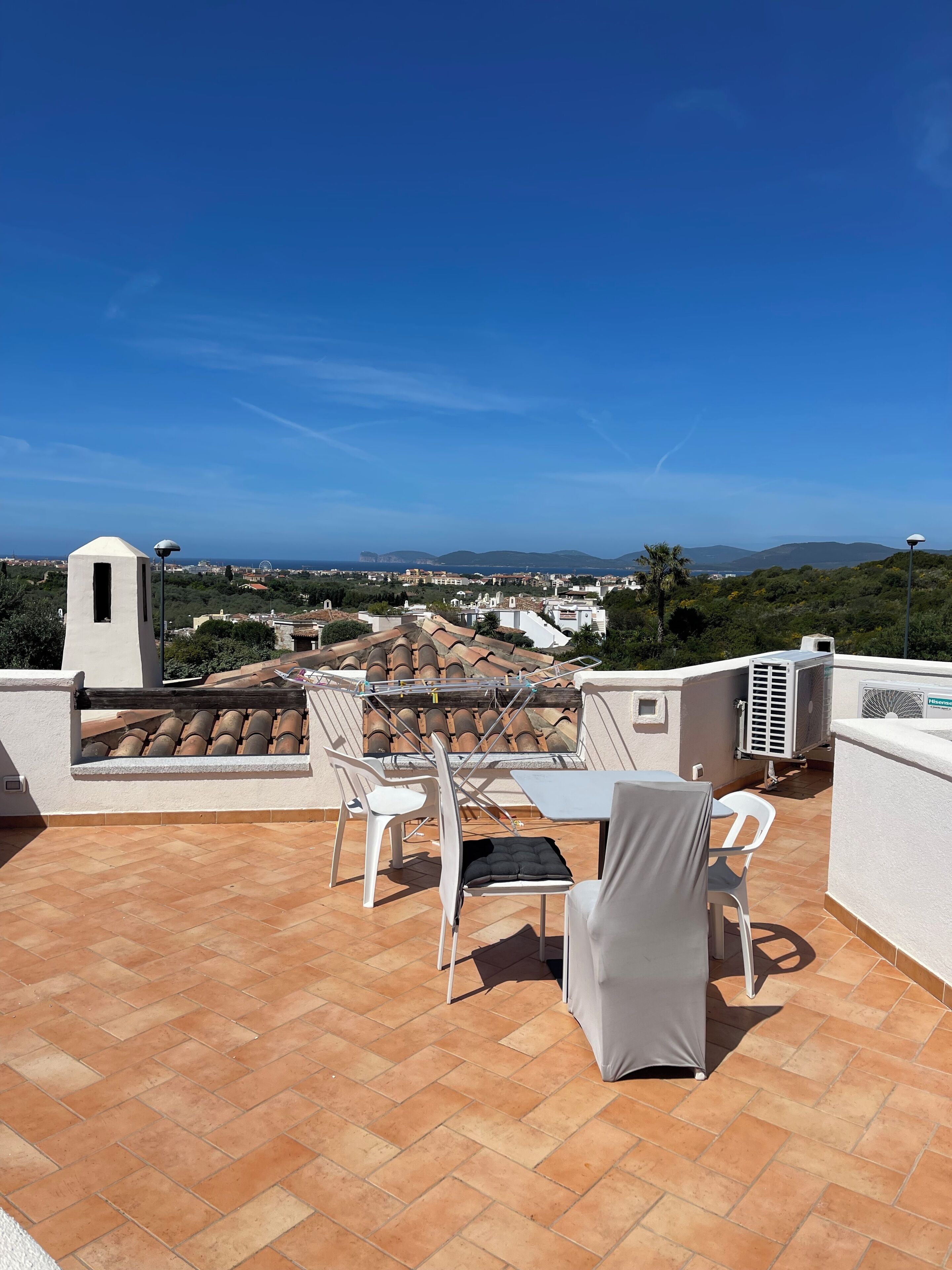 A rooftop terrace with a table and chairs, an air conditioning unit, and a view of the cityscape and hills.