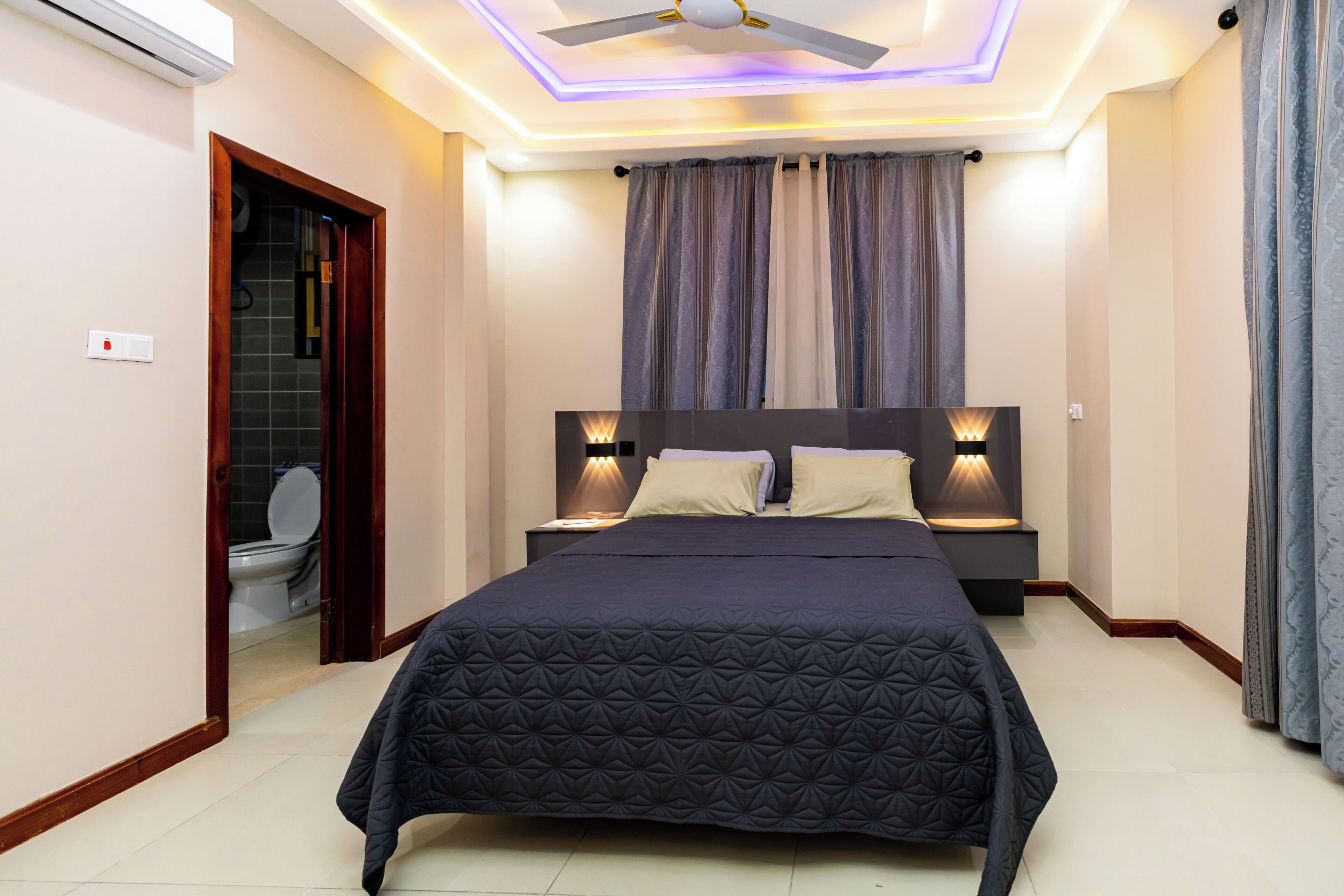 Une chambre à coucher avec un lit, des lampes de chevet, un ventilateur de plafond et une vue sur la salle de bain.