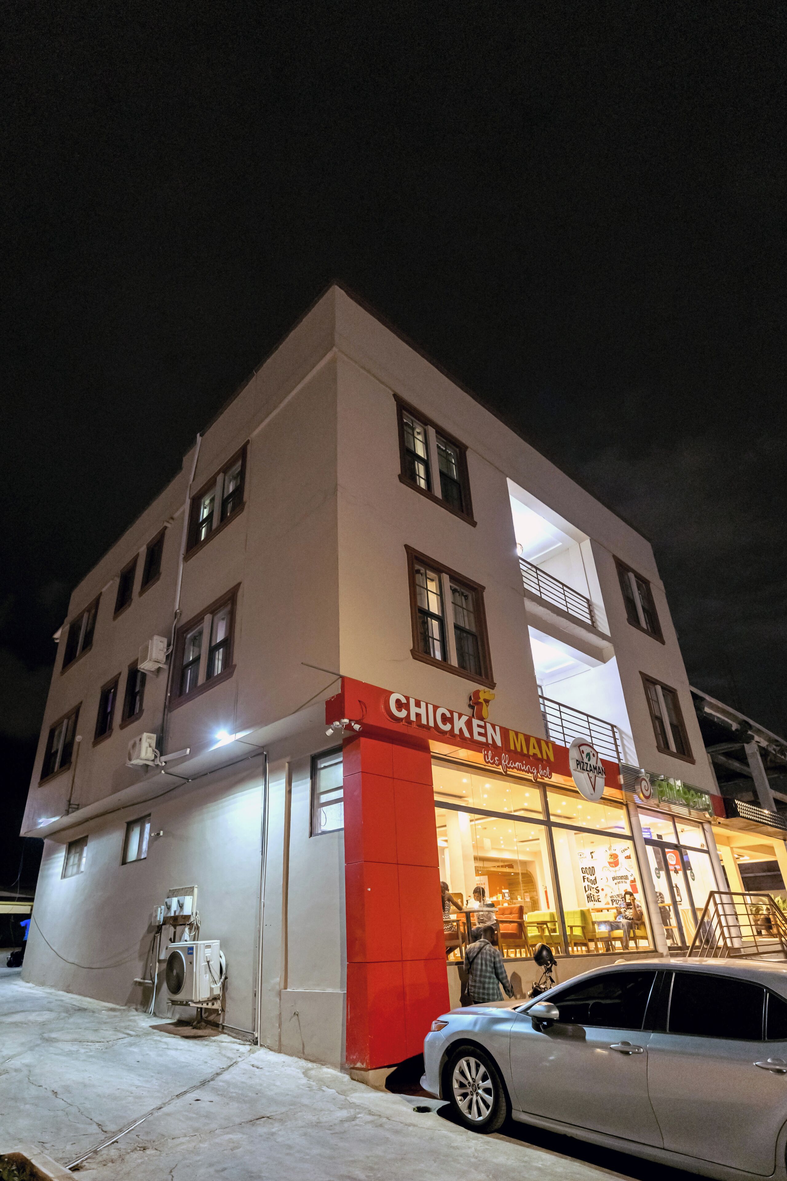 Un bâtiment sur lequel est apposée une enseigne indiquant « CHICKEN MAN », et une voiture garée devant.