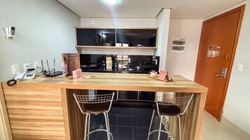 Una cocina compacta con encimera de madera, dos taburetes de bar, horno integrado y microondas.