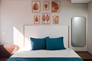 Un dormitorio moderno con una cama grande, dos almohadas azules y una obra de arte con hojas enmarcadas en la pared.