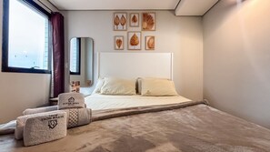 Habitación de hotel con cama, almohadas, un ventanal con cortinas, un espejo y una obra de arte en la pared.