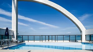 Une piscine sur le toit offrant une vue dégagée sur la mer, entourée d’une architecture moderne et d’une balustrade en verre.