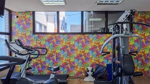 Une salle de sport équipée de matériel d’exercice, avec un mur en briques aux couleurs vives et de grandes fenêtres.