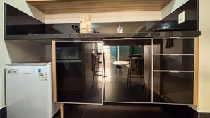 Eine Küche mit schwarzer Arbeitsplatte, einem weißen Kühlschrank und einem Essbereich mit einem Stuhl.