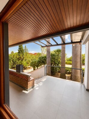 Ein geräumiger Balkon mit Holzboden, einem Ziegelpflanzgefäß und Blick auf tropische Bepflanzung.