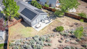 Ein Wohnhaus mit Solaranlage auf dem Dach, einer Terrasse mit Gartenmöbeln und einem angelegten Garten mit Sträuchern.