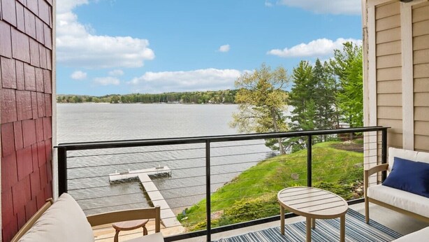 A balcony with a view of a lake, a small table, and a sofa. - Delton Dawn - Luxury at Delton Grand (Wisconsin Dells)