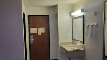 Una camera d'albergo con un letto, un bagno con lavandino e specchio, e una porta con dei bigliettini.